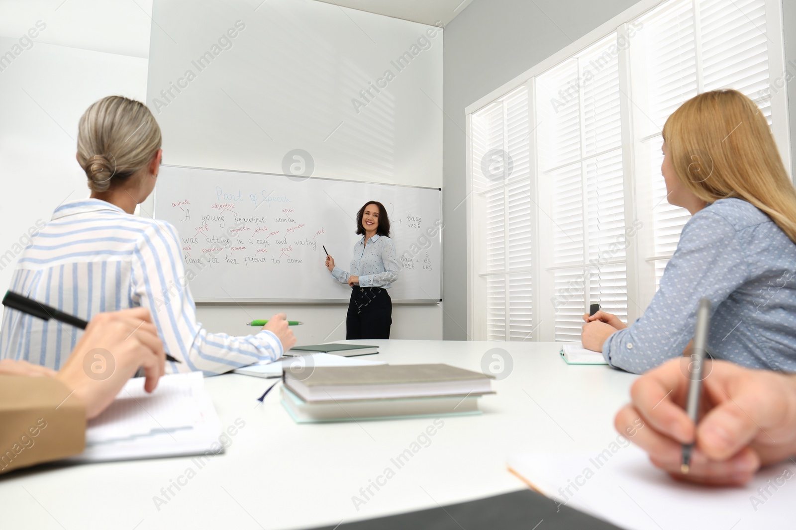 Photo of English teacher giving lesson near whiteboard in classroom