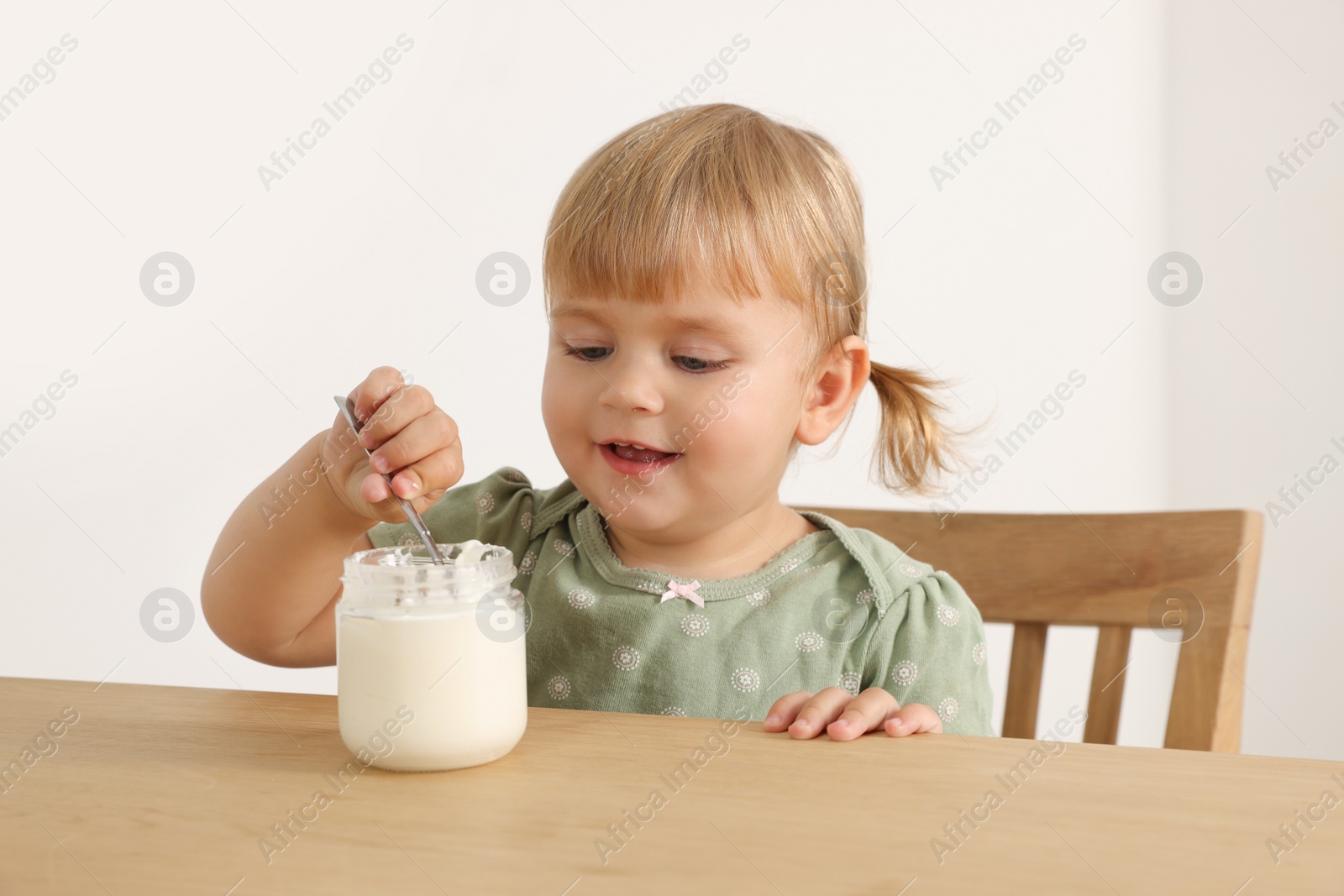 Photo of Cute little child eating tasty yogurt with spoon at wooden table indoors