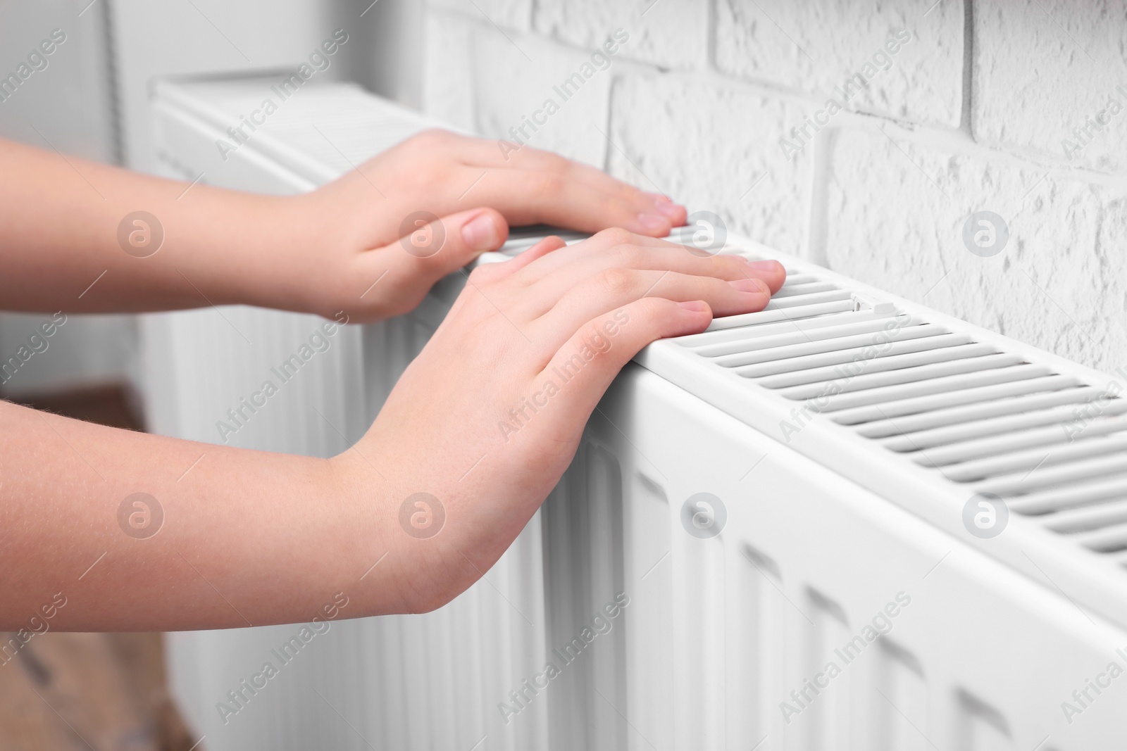 Photo of Girl warming hands on heating radiator indoors, closeup