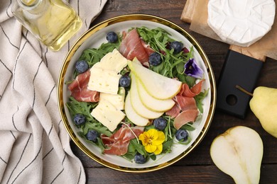 Photo of Tasty salad with brie cheese, prosciutto, blueberries and pear on wooden table, flat lay