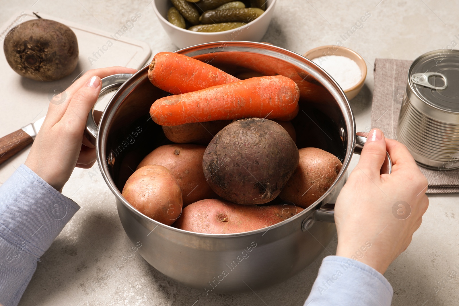 Photo of Woman holding pot with fresh vegetables at white table, closeup. Cooking vinaigrette salad