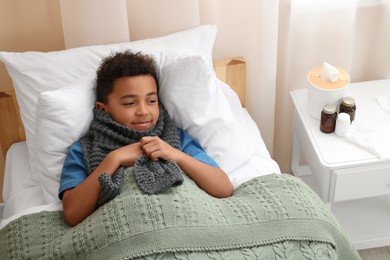 African-American boy with scarf lying in bed indoors, above view. Cold symptoms