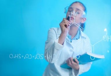 Schoolgirl writing chemistry formula on glass board against color background. Space for text