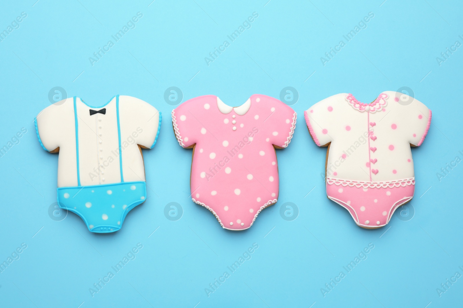 Photo of Cute tasty cookies in shape of baby's onesies on light blue background, flat lay