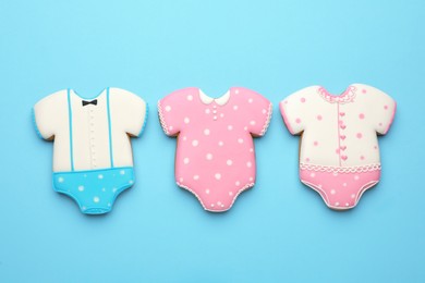 Cute tasty cookies in shape of baby's onesies on light blue background, flat lay