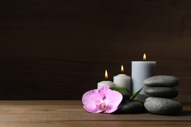 Photo of Spa stones, orchid flower, burning candles and bamboo sprout on wooden table. Space for text