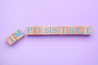 Motivation concept. Changing word from Impossible into Possible by removing wooden cubes on violet background, flat lay