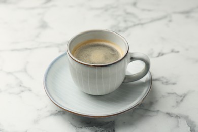 Photo of Tasty coffee in cup and saucer on white marble table, closeup