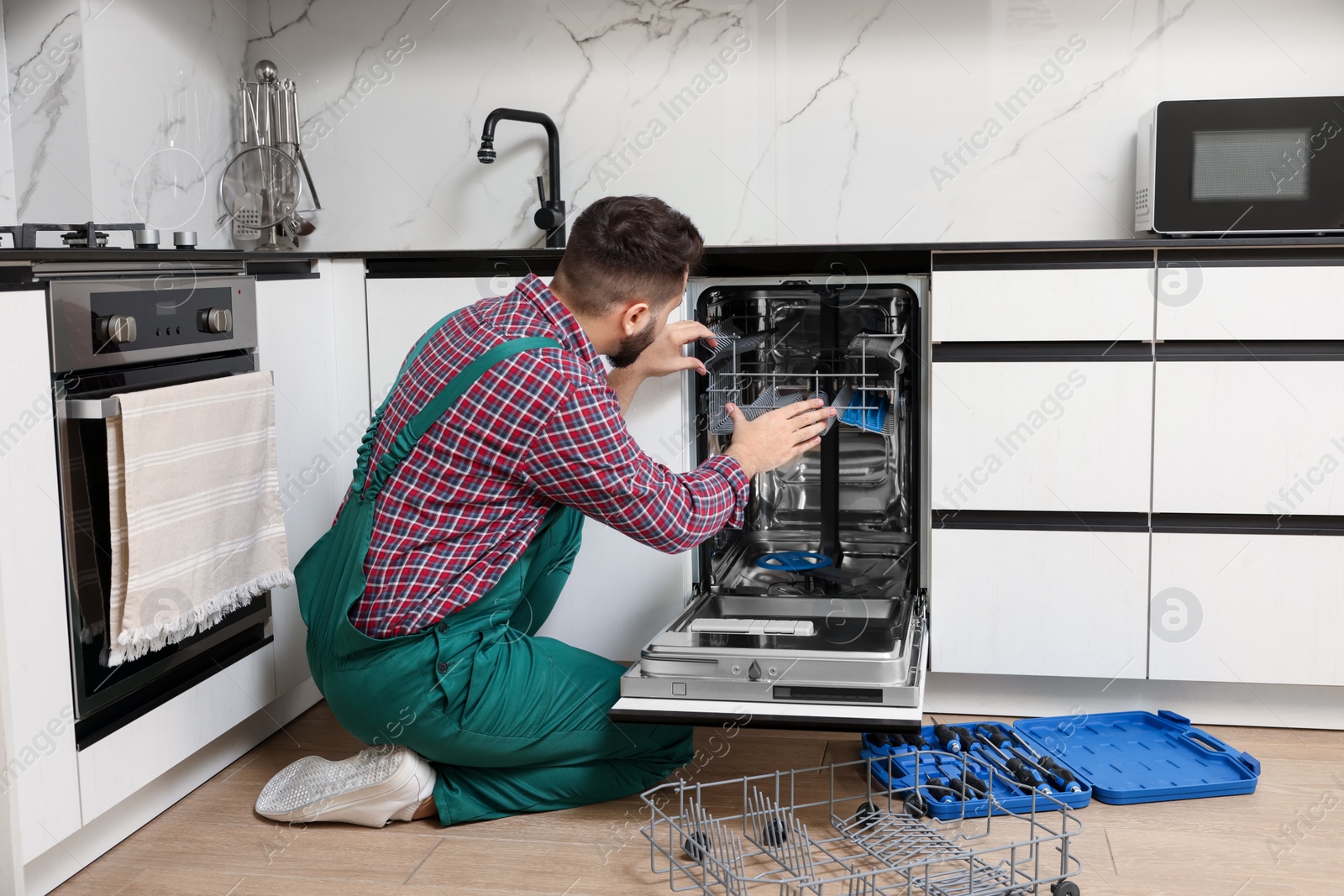 Photo of Serviceman repairing dishwasher cutlery rack in kitchen, back view