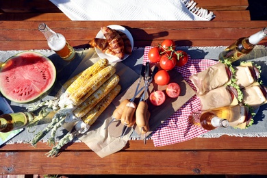 Bottles of beer and tasty food on wooden table, top view. Camping season