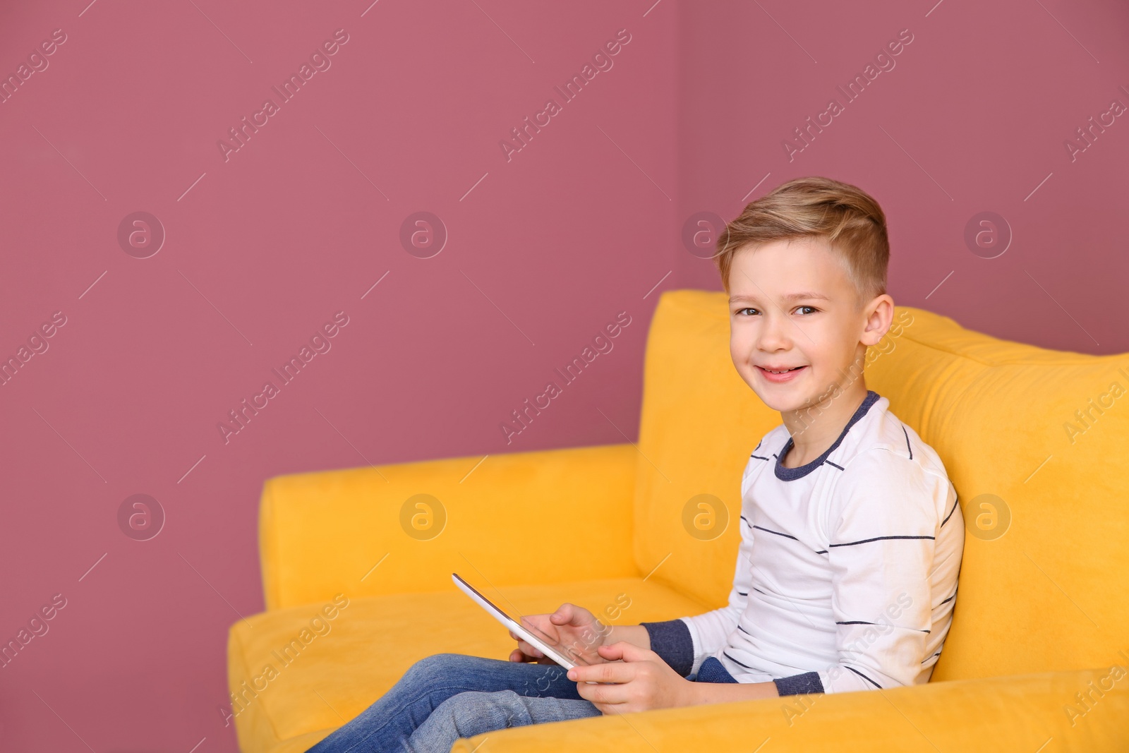 Photo of Cute little boy sitting on sofa with tablet computer, indoors