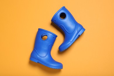 Photo of Bright blue rubber boots on orange background, top view