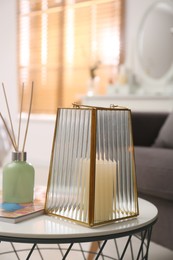 Stylish holder with burning candle and reed air freshener on table in room