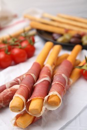 Photo of Delicious grissini sticks with prosciutto and snacks on white table, closeup