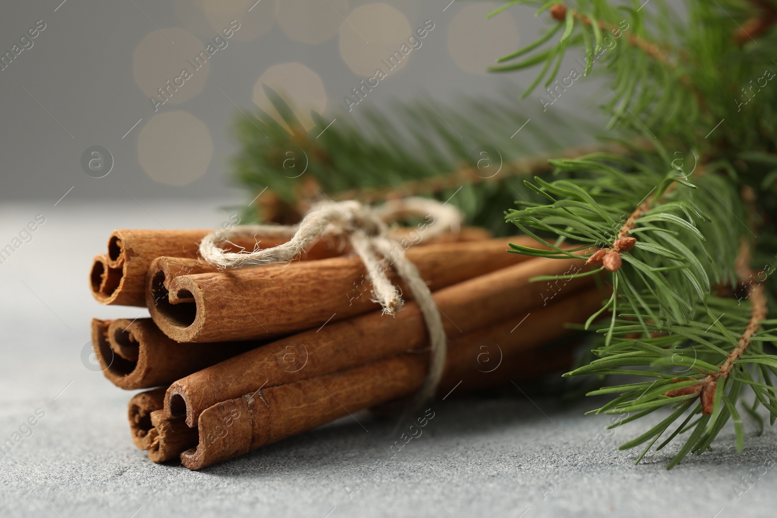 Photo of Bunch of cinnamon sticks and fir branches on grey textured table, closeup