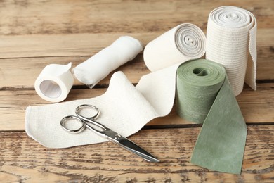 Photo of Medical bandage rolls, sticking plaster and scissors on wooden background