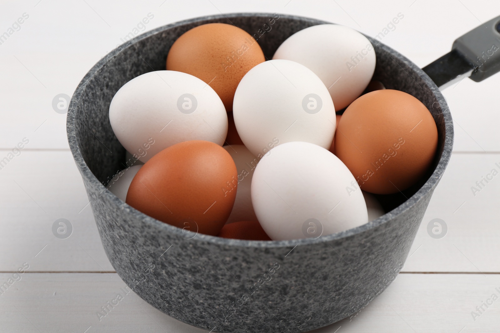 Photo of Unpeeled boiled eggs in saucepan on white wooden table, closeup