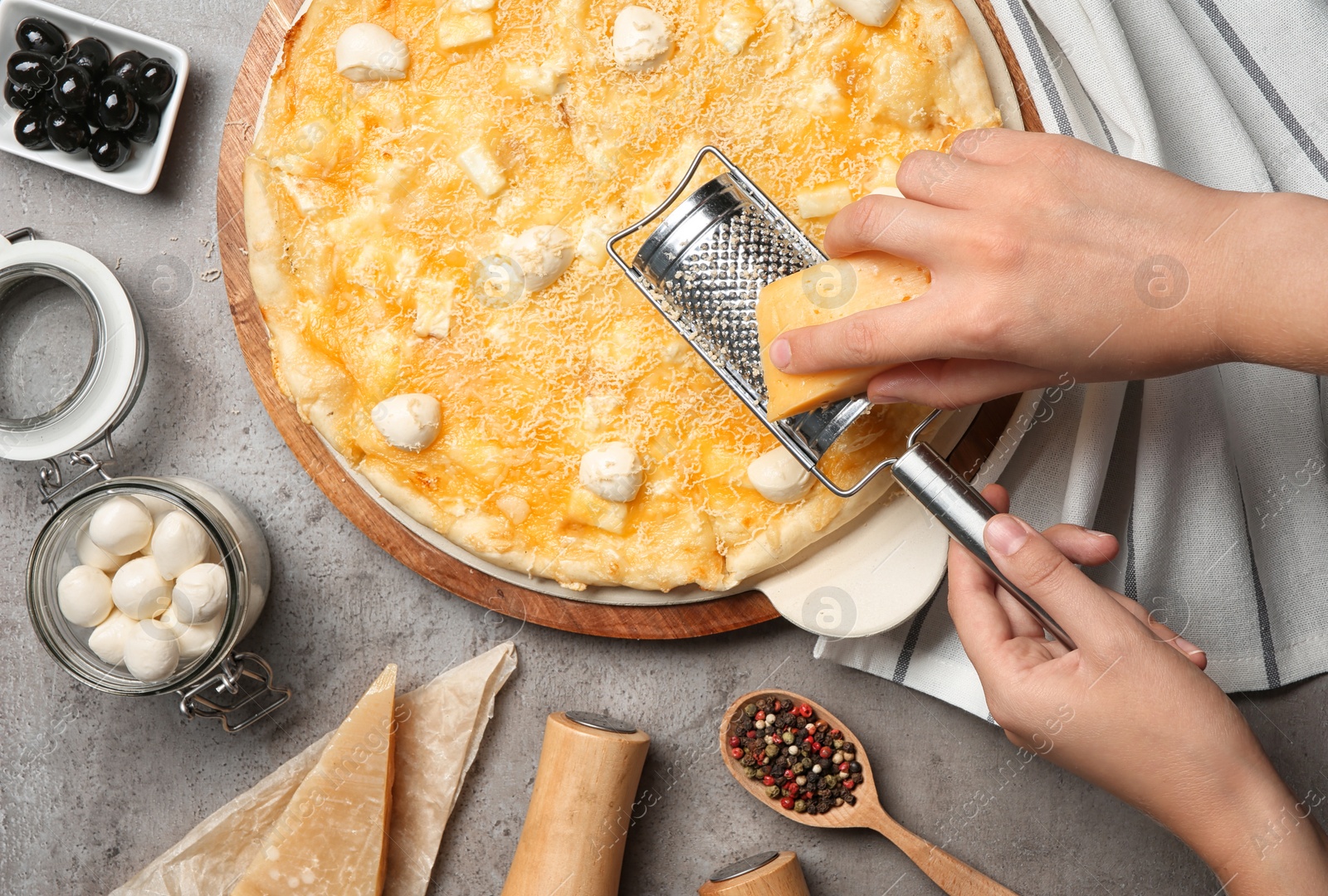 Photo of Woman grating cheese onto homemade pizza on table, top view