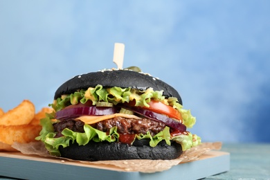 Photo of Board with black burger and french fries on table, closeup. Space for text