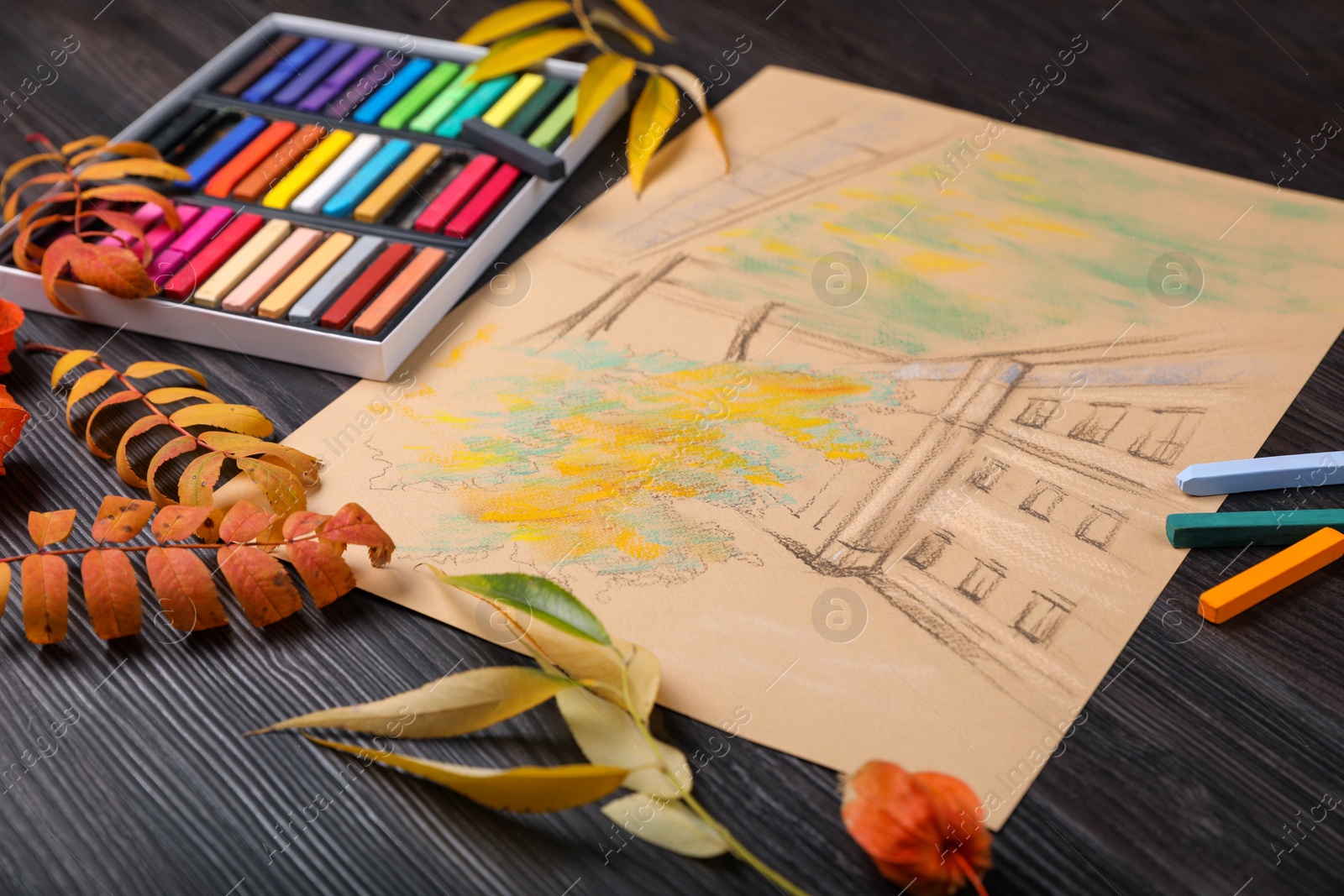 Photo of Colorful pastels, beautiful drawing of building and autumn leaves on wooden table