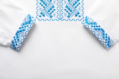 Photo of Beautiful white shirt with light blue Ukrainian national embroidery, top view. Space for text