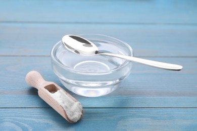 Photo of Bowl of fructose syrup and scoop with powder on light blue wooden table