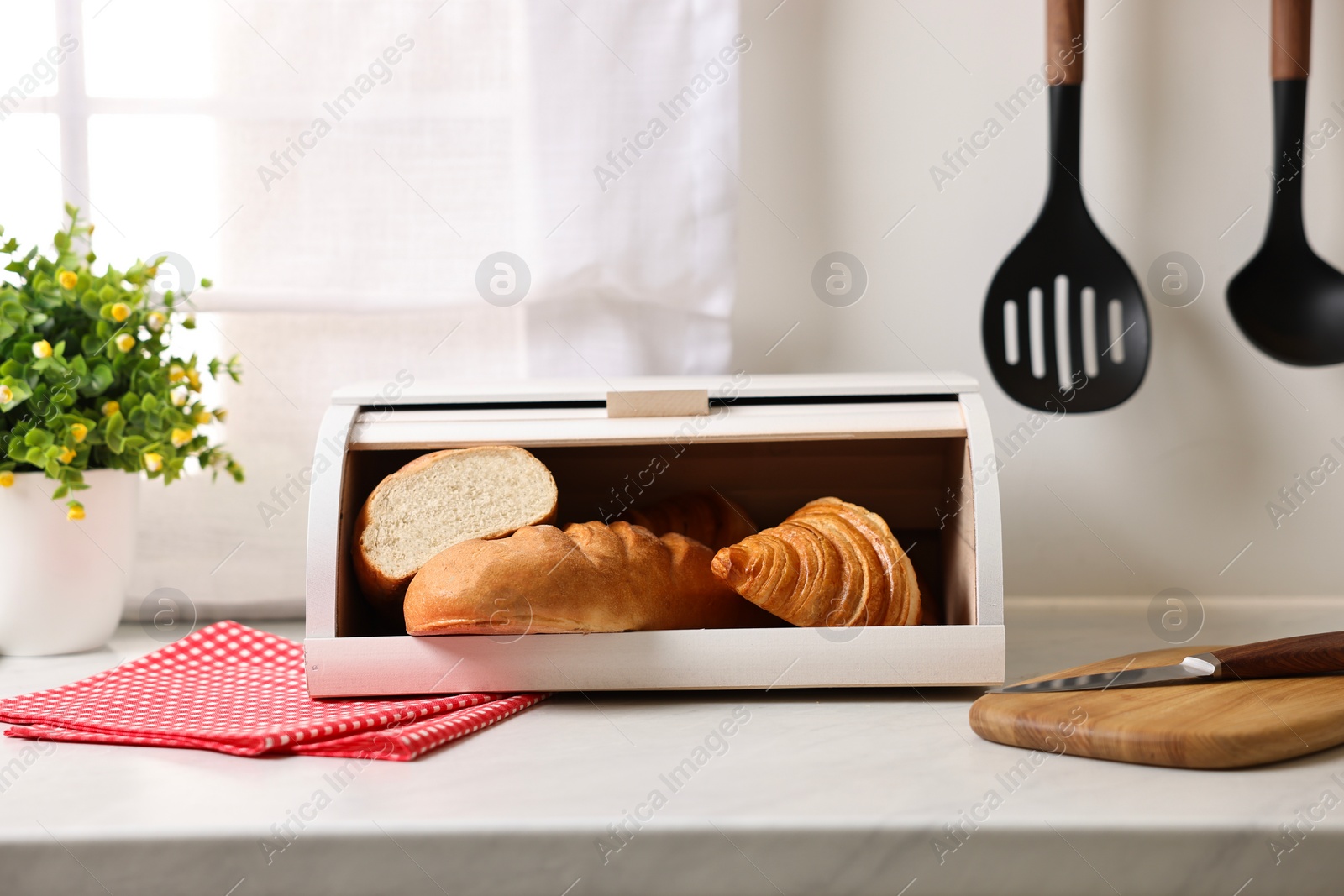 Photo of Wooden bread basket with freshly baked loaves on white marble table in kitchen