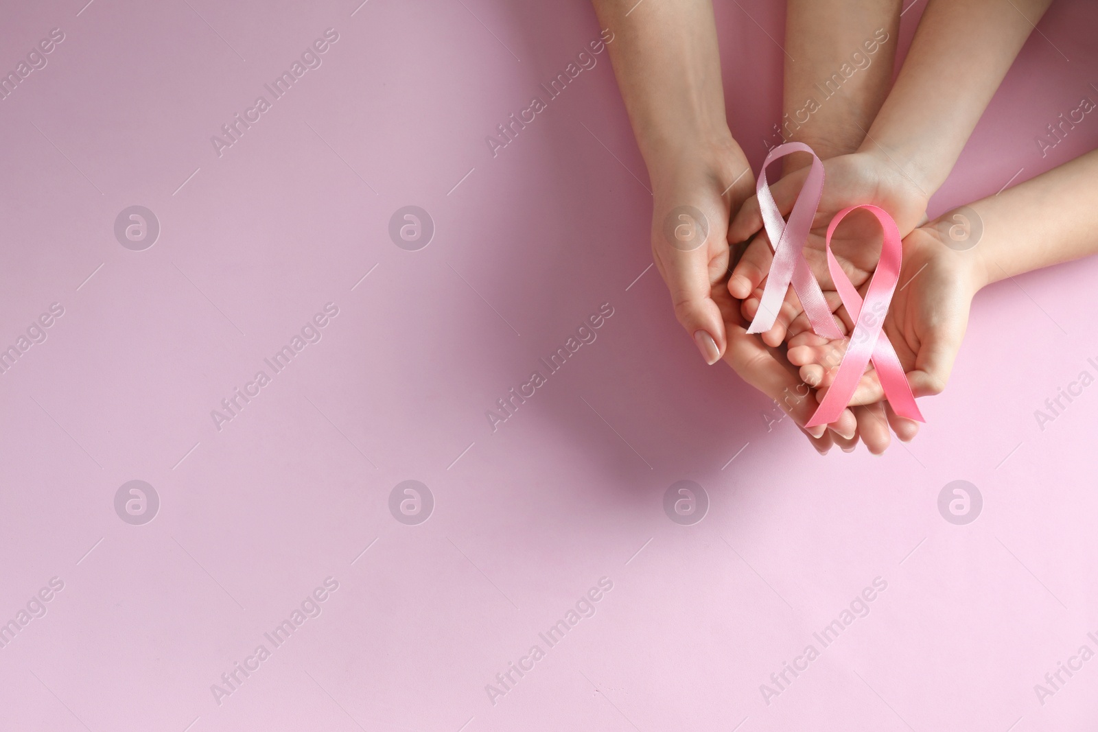 Photo of Woman and child holding pink ribbon on color background, top view with space for text. Breast cancer awareness