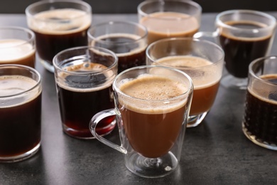 Many cups of different aromatic hot coffee on grey background