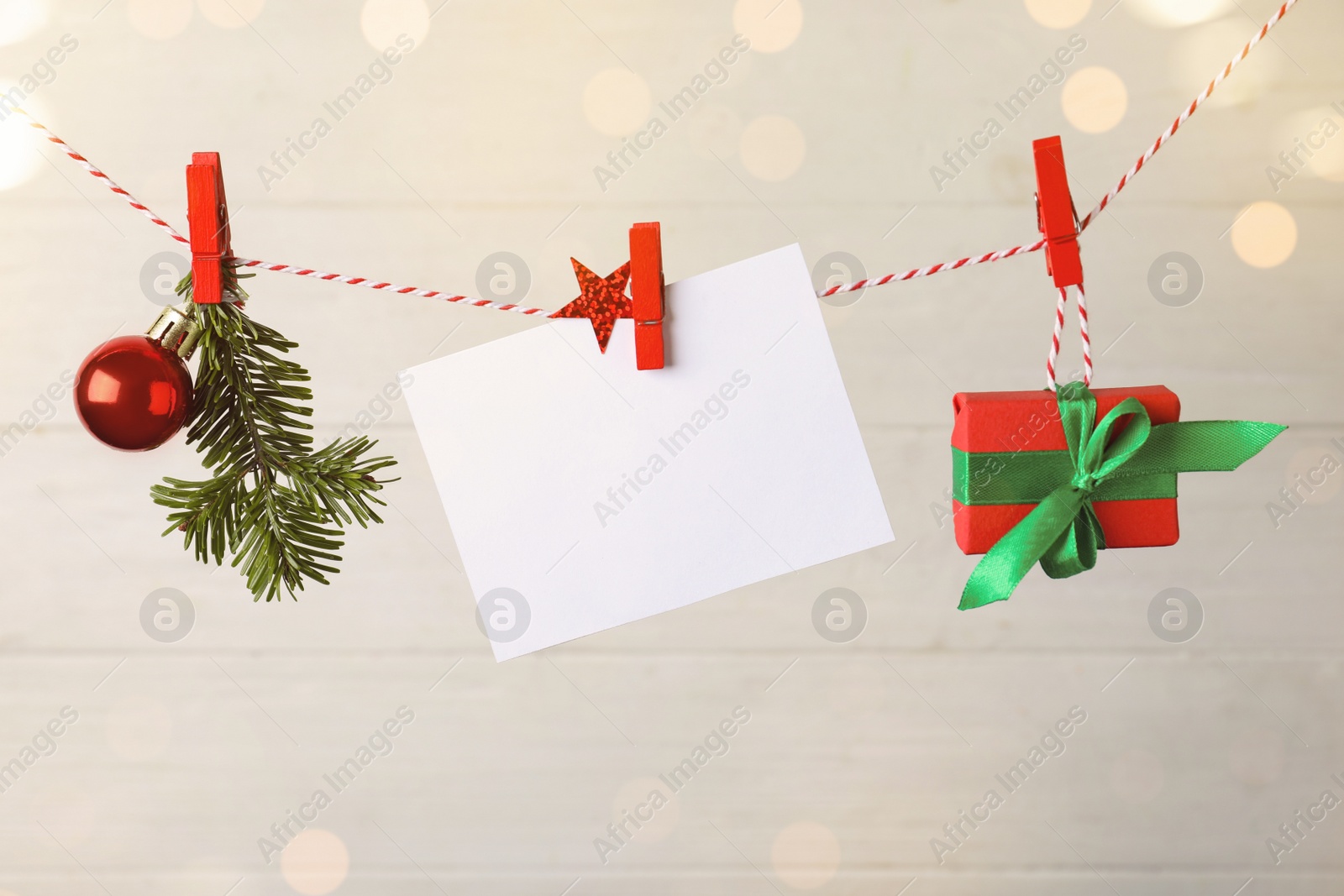 Photo of Blank Christmas card and festive decor on rope against white background, space for text