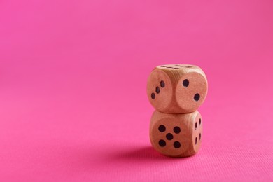Photo of Two stacked wooden game dices on pink background, closeup. Space for text