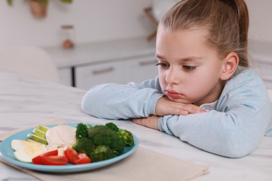 Photo of Cute little girl refusing to eat dinner in kitchen