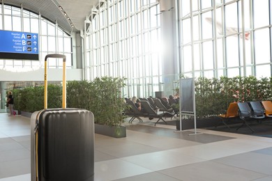 Image of Stylish black suitcase in waiting area at airport terminal