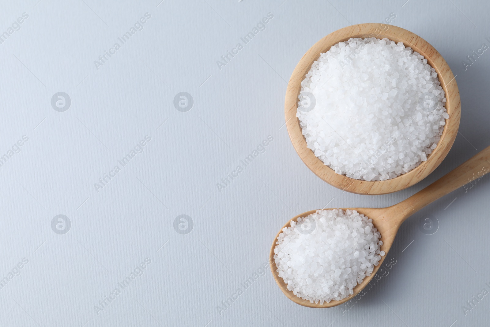 Photo of Organic white salt in bowl and spoon on light grey background, top view. Space for text