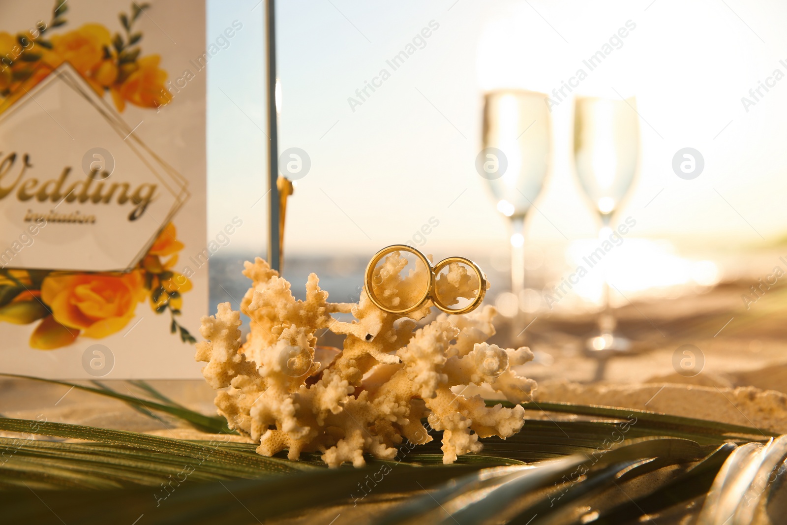 Photo of Coral with gold rings and wedding invitation on sandy beach