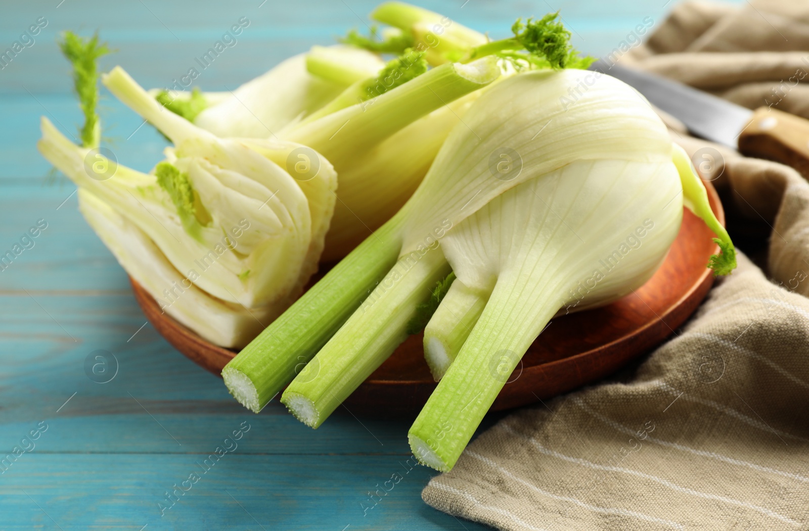 Photo of Whole and cut fennel bulbs on light blue wooden table, closeup