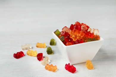 Bowl with delicious jelly bears on light wooden table. Space for text