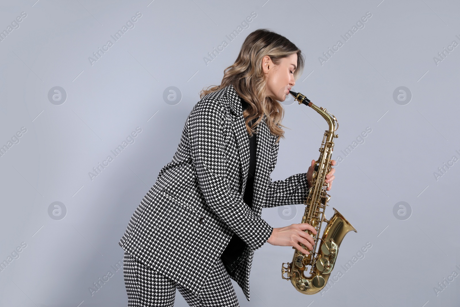 Photo of Beautiful young woman in elegant suit playing saxophone on grey background