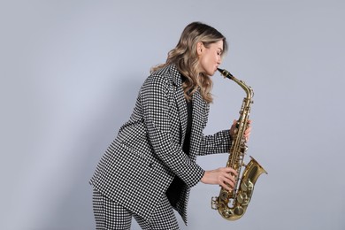 Photo of Beautiful young woman in elegant suit playing saxophone on grey background