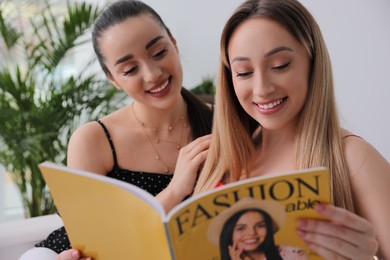 Photo of Happy women reading fashion magazine together indoors