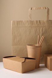 Photo of Eco friendly food packaging. Paper containers, bag and straws on white table against beige background