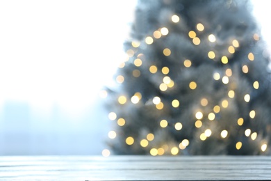 Photo of Blurred view of beautiful Christmas tree with yellow lights near window indoors, focus on wooden table. Space for text