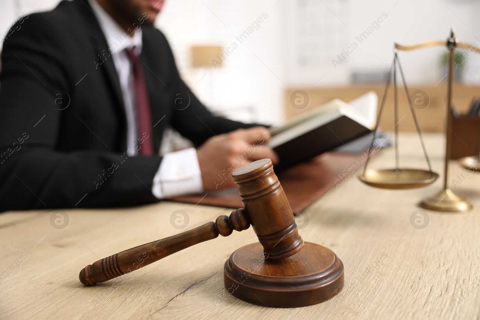 Photo of Lawyer reading book at table in office, focus on gavel