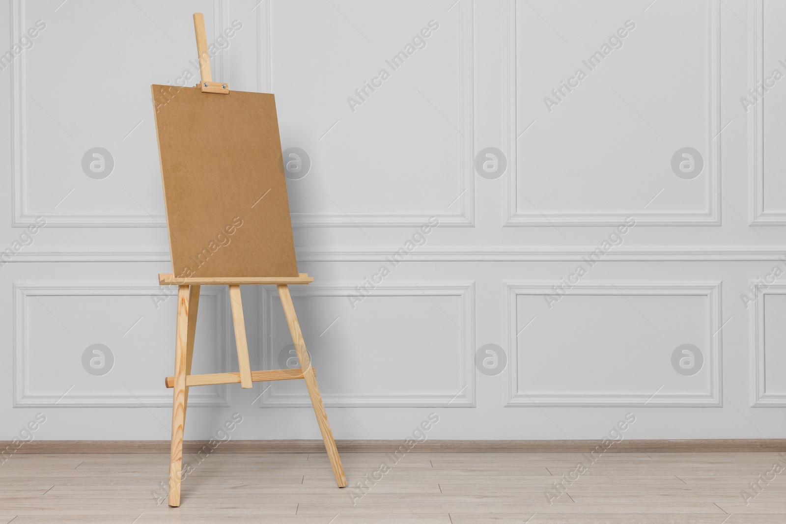 Photo of Wooden easel with blank board near white wall indoors. Space for text