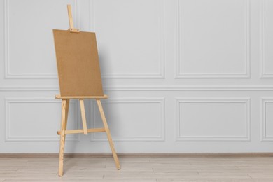 Photo of Wooden easel with blank board near white wall indoors. Space for text
