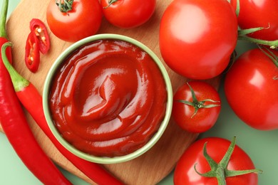 Photo of Bowl of tasty ketchup and ingredients on green table, flat lay