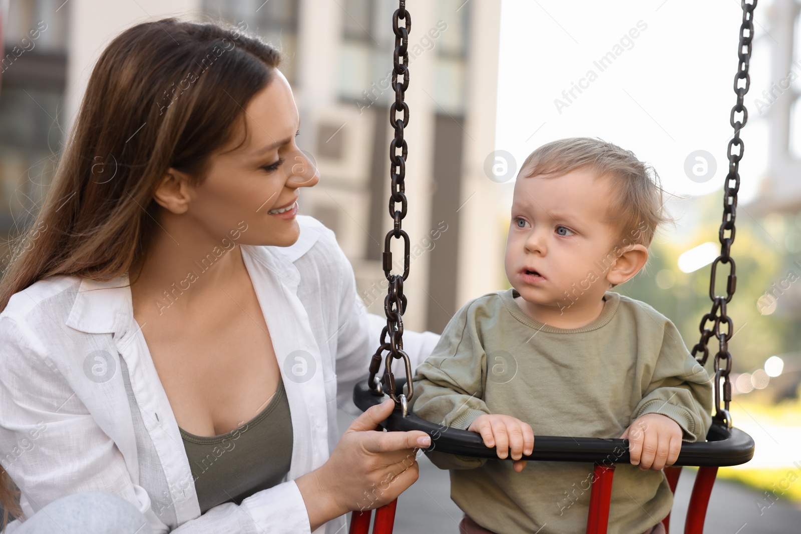 Photo of Happy nanny and cute little boy on swing outdoors