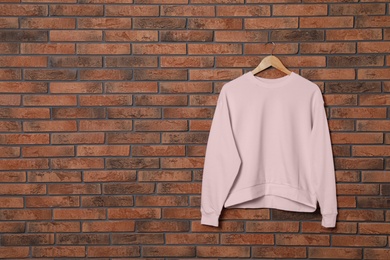 Photo of Hanger with new female sweater on brick wall, mock up for design