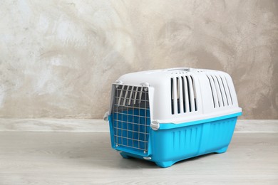 Light blue pet carrier on floor near beige wall, space for text