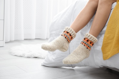 Woman wearing knitted socks on bed indoors, closeup. Warm clothes